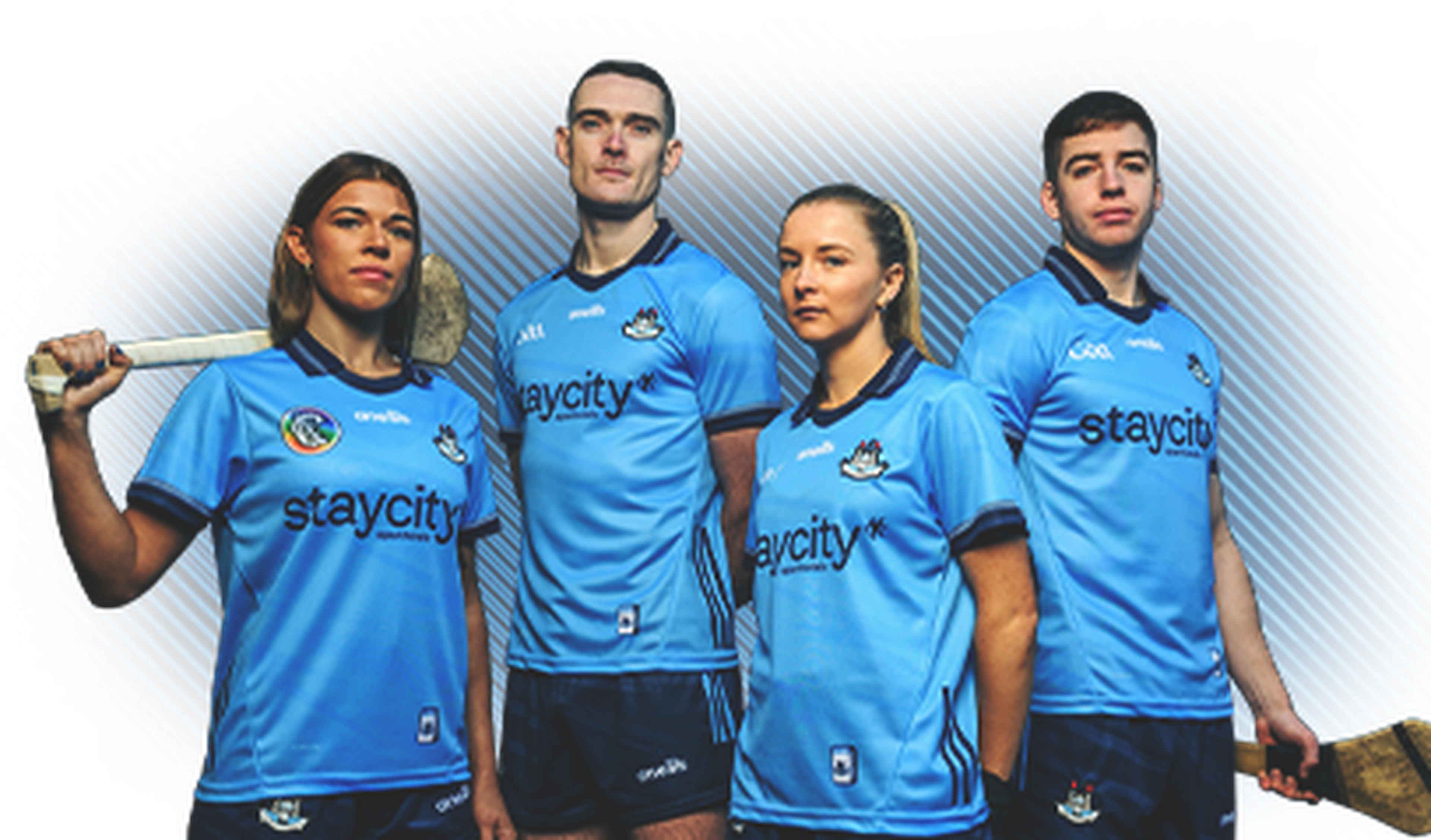 Four athletes in blue sports jerseys holding hurling sticks, standing confidently against a textured background.
